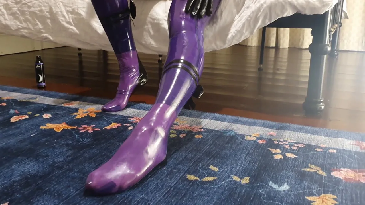 Slim girl in purple latex bodysuit gets on bed in bedroom