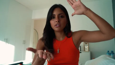 Asian brunette with shoulder tattoo talks and gestures in bedroom
