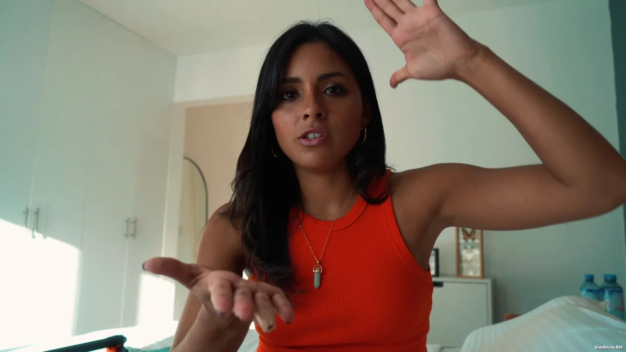 Asian brunette with shoulder tattoo talks and gestures in bedroom